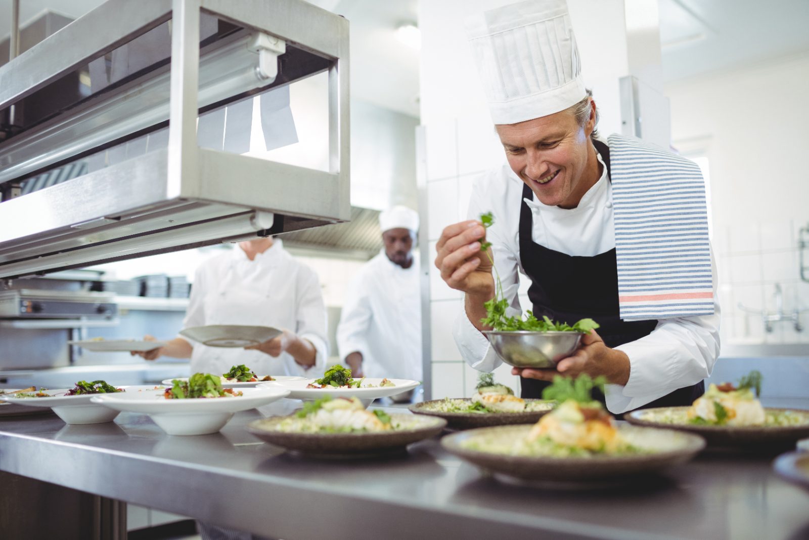 Chef plating dishes at the order station while training new seasonal kitchen staff